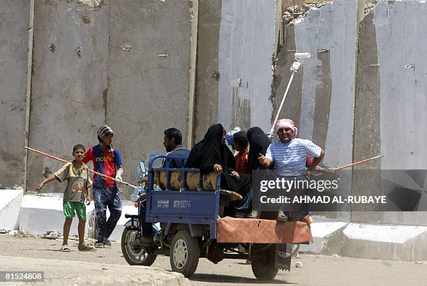 Iraqis ride in the back of a 'satuta', a cart pulled by a motorcycle, as they pass Iraqi boys adding a splash of colour to a cement block security...