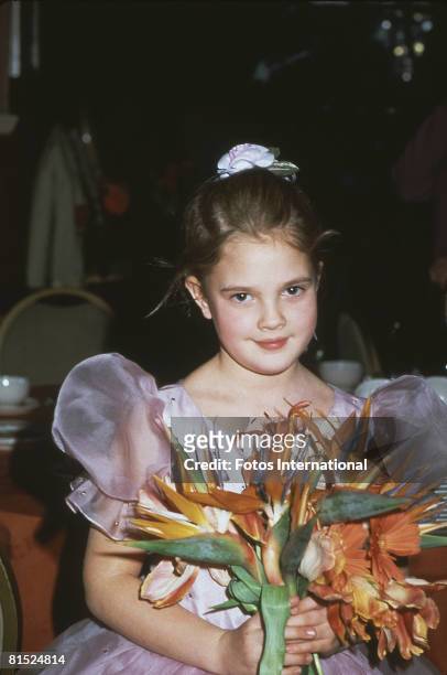 American child actress Drew Barrymore holds a bouquet of flowers as she attends the 40th Annual Golden Globe Awards in support of her film 'E.T. The...