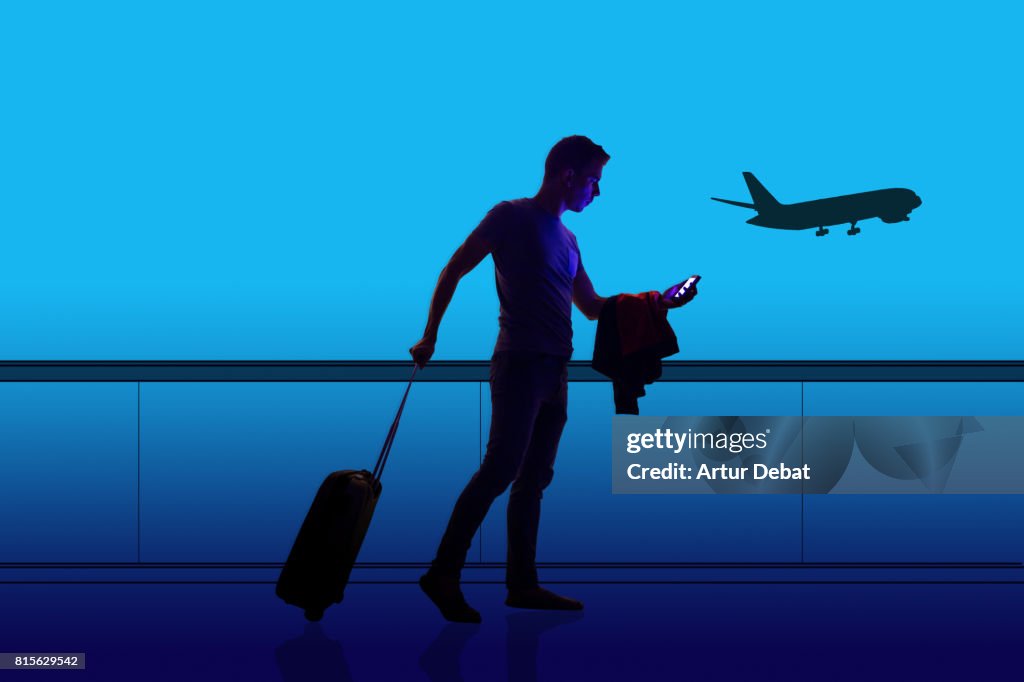 Silhouette of a guy checking his smartphone ready to departure on a airport at night with illustration effect during a travel with trolley suitcase using application technology to get information about the trip.