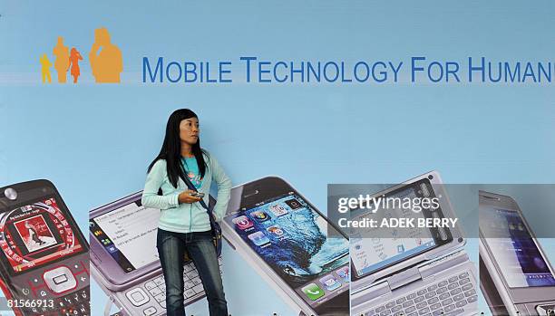 Woman stands in front of a huge billboard at a local IT fair titled "Pameran Akbar Teknologi Seluler" in Jakarta on June 14, 2008. Indonesia's...