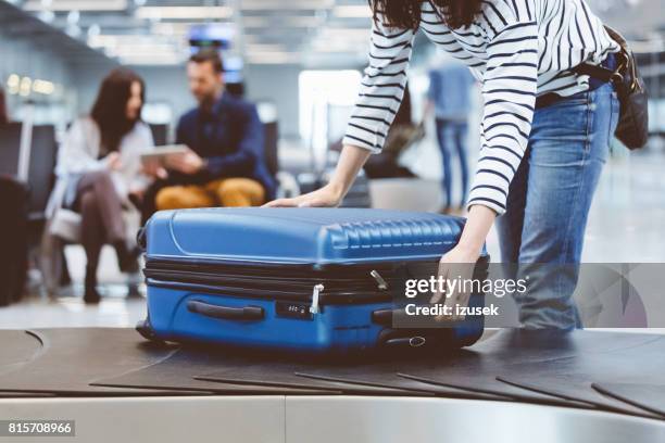 female traveler picking up suitcase from baggage claim line - bagagem imagens e fotografias de stock