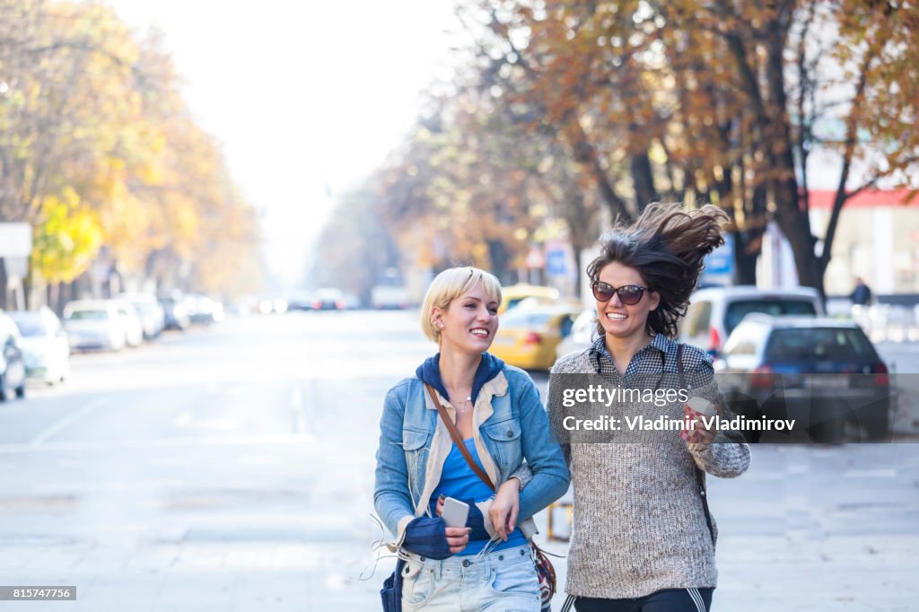 Two cheerful young women walking on street and having fun