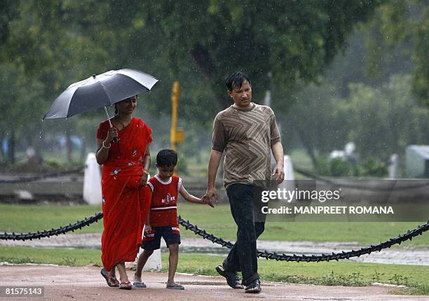 An Indian family walks on India Gate lawns during a heavy downpour of rain in New Delhi on June 15, 2008. Delhiites woke up to a pleasant day, with...