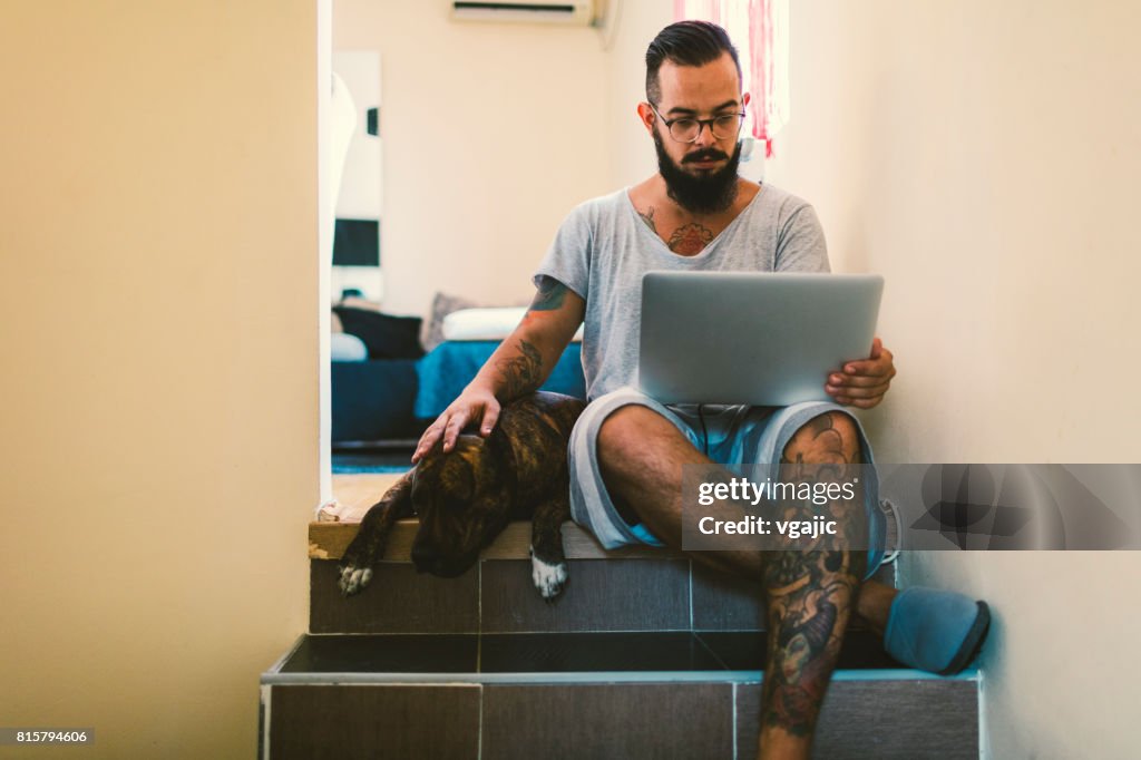 Uomo che usa laptop a casa con il suo cane accanto a lui