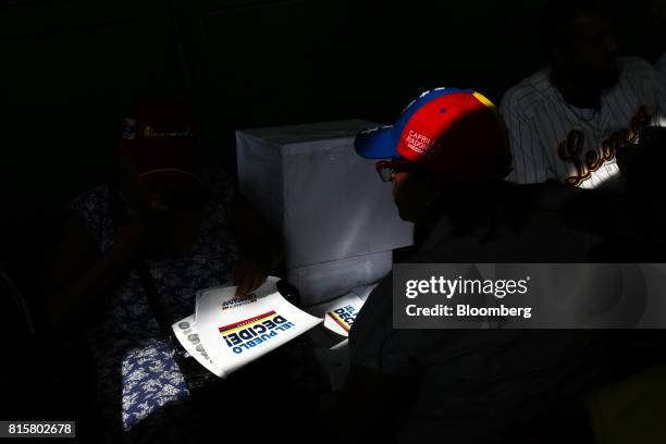 Volunteer wearing a cap in the colors of the Venezuelan flag sits in front of a ballot box during a symbolic Venezuelan plebiscite in Caracas,...