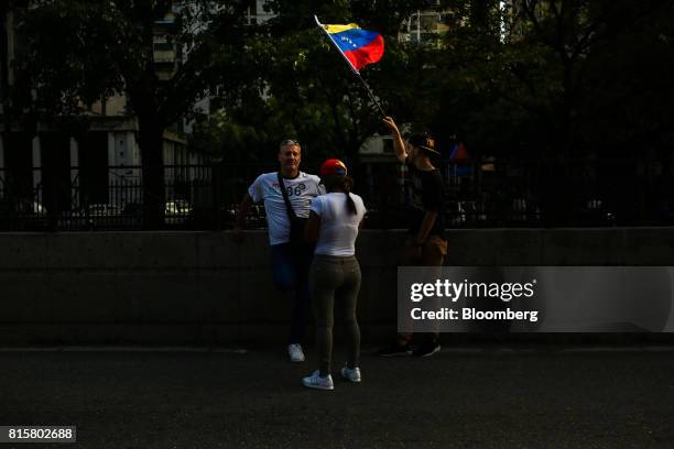 People stand on a street as a man waves a Venezuelan flag during a symbolic Venezuelan plebiscite in Caracas, Venezuela, on Sunday, July 16, 2017....