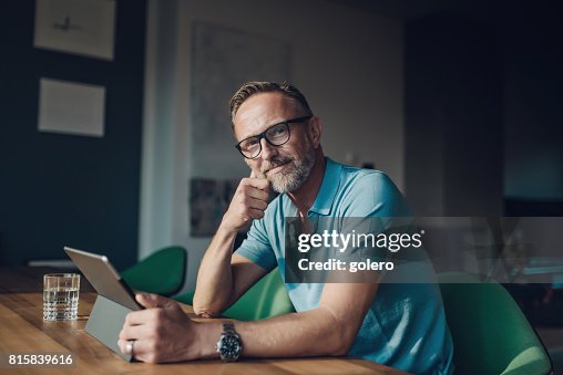 Hübscher bärtigen midaged Mann am Tisch mit digital-Tablette Hübscher bärtigen midaged Mann am Tisch mit digital-Tablette