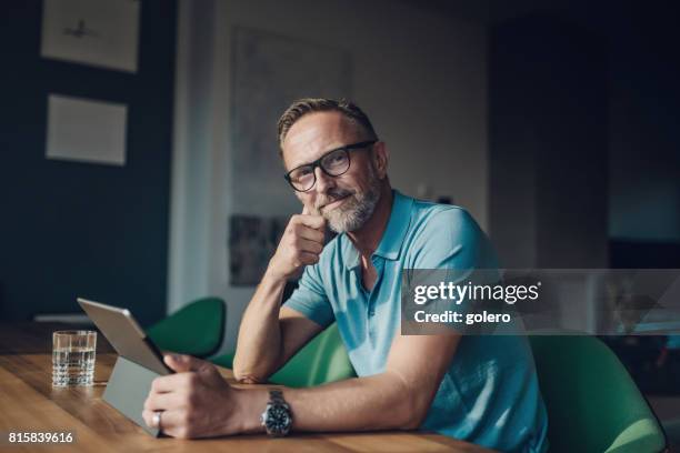 handsome bearded midaged man at table with digital tablet - independent house stock pictures, royalty-free photos & images