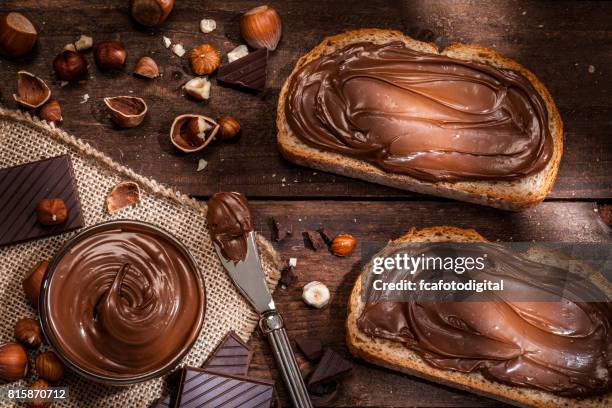 chocolate and hazelnut spread on bread slices shot on rustic wooden table - spread imagens e fotografias de stock