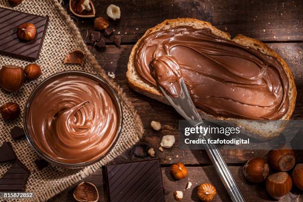 chocolate and hazelnut spread on bread slice shot on rustic wooden table - chocolate spread stock pictures, royalty-free photos & images