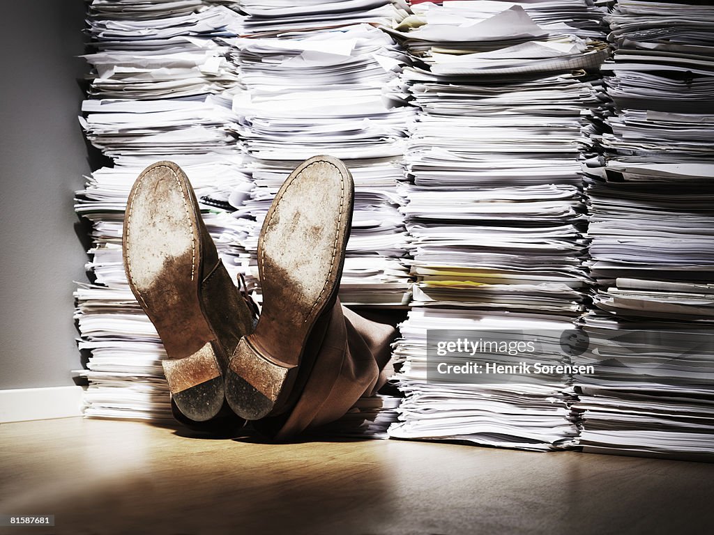 A pair of feet sticking out from under a pile of papers.
