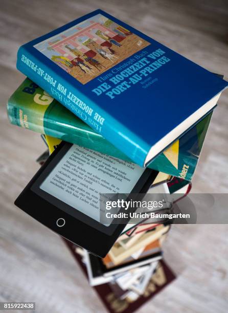 Symbol photo on the topics of literature, reading, eBook, books, leisure, vacation, etc. The photo shows an eBook between stacked books.