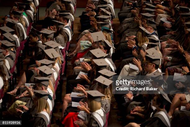 Young graduates wearing rented gowns and mortarboards applaud a speech in the central hall of their university during their graduation ceremony, on...
