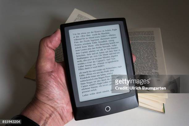 Symbol photo on the topics of literature, reading, eBook, books, leisure, vacation, etc. The photo shows a hand with an eBook and a bound book.