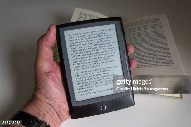 Symbol photo on the topics of literature, reading, eBook, books, leisure, vacation, etc. The photo shows a hand with an eBook and a bound book.