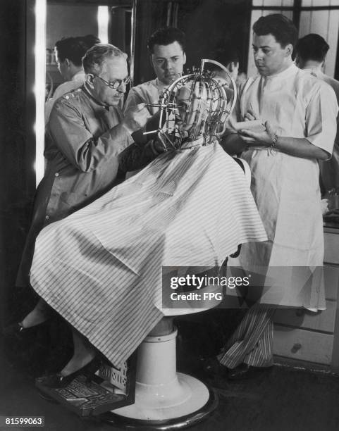 Hollywood cosmetics expert Max Factor takes precise measurements of a young woman's head and face with a 'Beauty Calibrator', device, circa 1932. The...