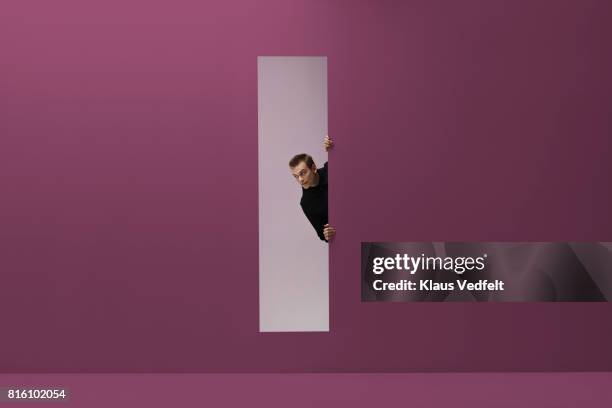 man peeking threw rectangular opening in coloured room - aparición conceptos fotografías e imágenes de stock