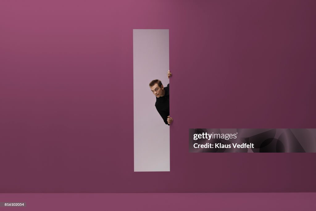 Man peeking threw rectangular opening in coloured room