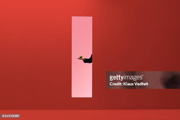 man reaching hand out threw rectangular opening in coloured wall and holding apple - veleiding stockfoto's en -beelden