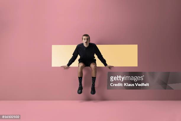 man sitting on the edge of rectangular opening in coloured wall - change socks stockfoto's en -beelden