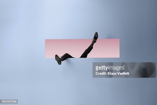 feet of businessman, sticking out rectangular opening in coloured wall - hinunter bewegen stock-fotos und bilder