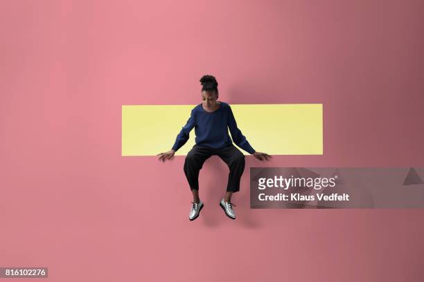 woman sitting on the edge of rectangular opening in coloured wall and looking down - sitzen stock-fotos und bilder