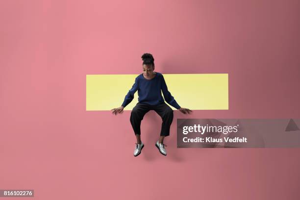 woman sitting on the edge of rectangular opening in coloured wall and looking down - mirar hacia abajo fotografías e imágenes de stock