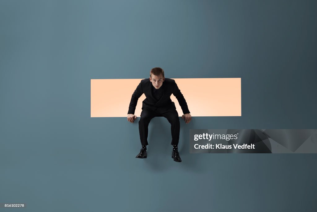 Man sitting on the edge of rectangular opening in coloured wall