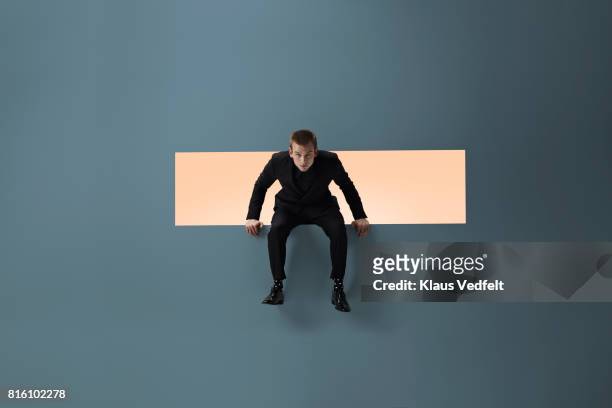 man sitting on the edge of rectangular opening in coloured wall - leaning stock pictures, royalty-free photos & images