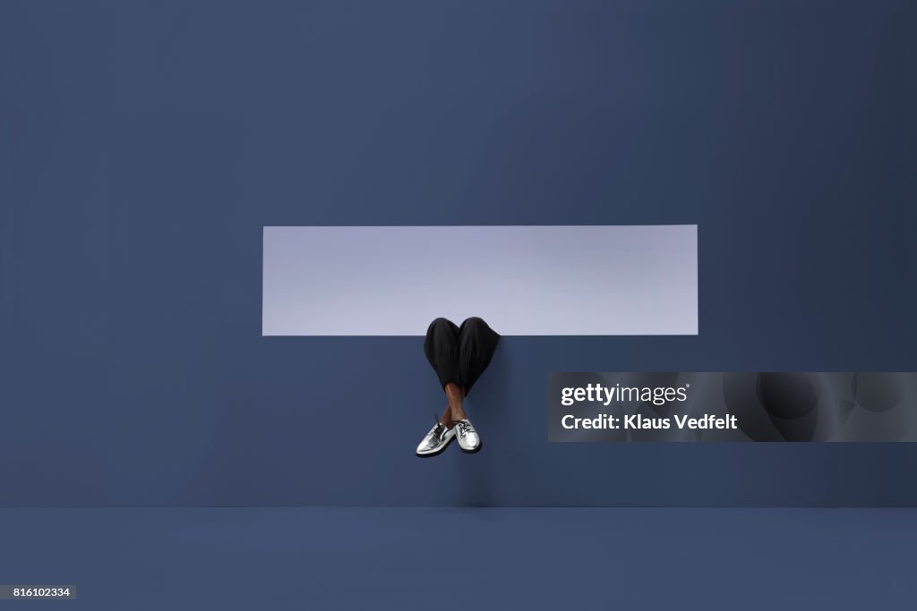 Womans legs sticking out of rectangular opening in coloured wall and looking up