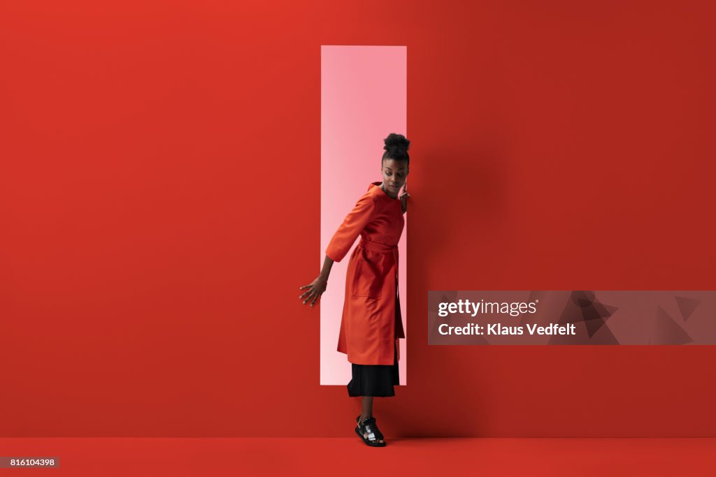 Woman coming out of rectangular opening in coloured wall