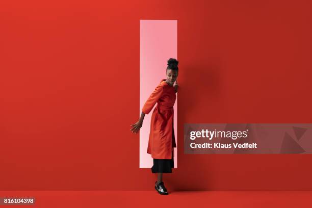 woman coming out of rectangular opening in coloured wall - rode overjas stockfoto's en -beelden