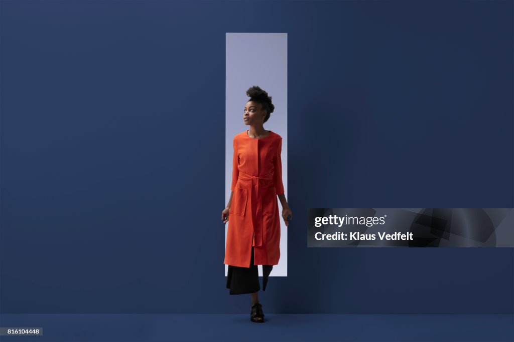 Woman coming out of rectangular opening in coloured wall