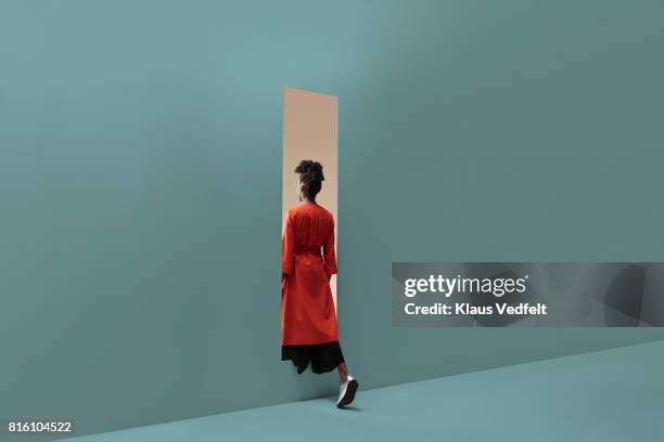 woman walking into rectangular opening in coloured wall - groene overjas stockfoto's en -beelden