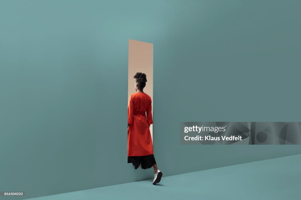 Woman walking into rectangular opening in coloured wall
