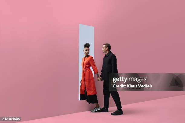 woman & man holding hands, approaching rectangular opening in coloured wall - acercarse fotografías e imágenes de stock