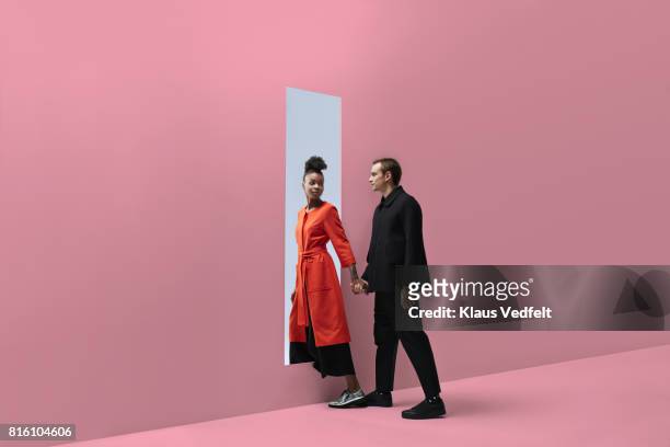 woman & man holding hands, approaching rectangular opening in coloured wall - ideal wife stock pictures, royalty-free photos & images
