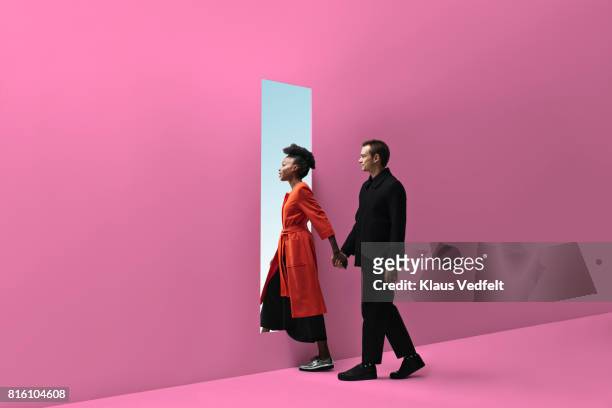 woman & man holding hands, approaching rectangular opening in coloured wall - entrando fotografías e imágenes de stock