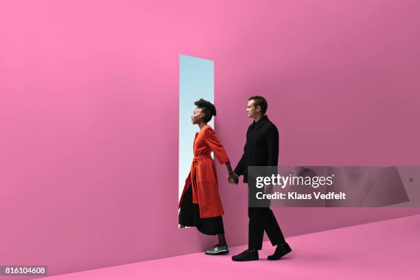 woman & man holding hands, approaching rectangular opening in coloured wall - entrare foto e immagini stock