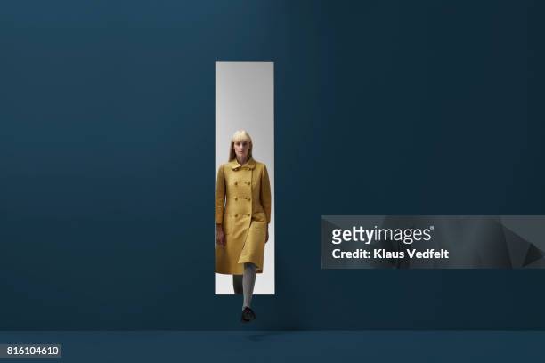 woman coming out of rectangular opening in coloured wall - overcoat stock pictures, royalty-free photos & images