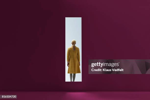 woman walking into rectangular opening in coloured wall - manteau jaune photos et images de collection