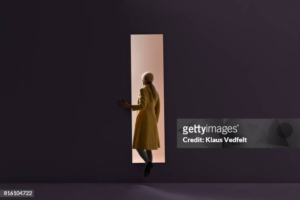 woman walking into rectangular opening in coloured wall - anticipation stock pictures, royalty-free photos & images
