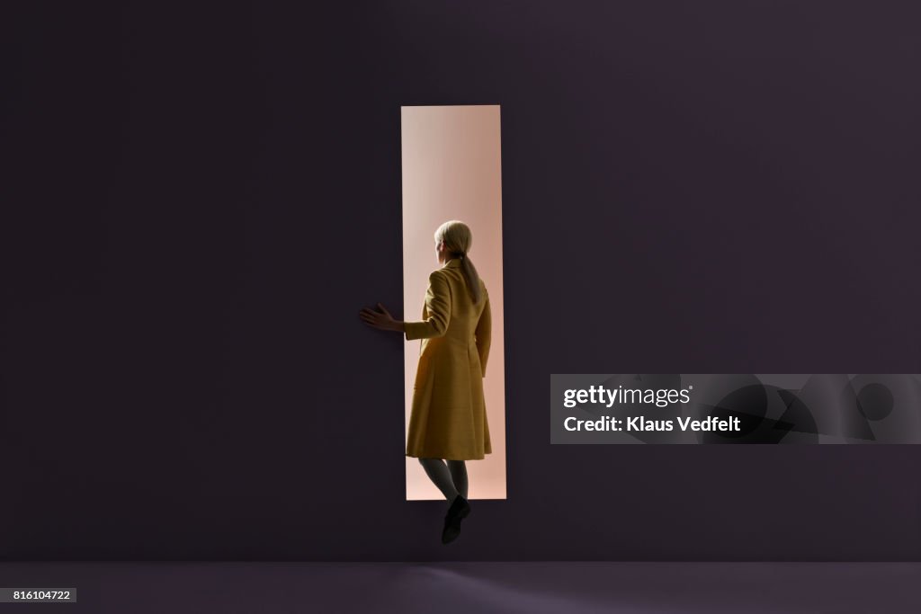 Woman walking into rectangular opening in coloured wall