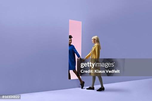 Two women holding hands, walking threw rectangular opening in coloured wall Two women holding hands, walking threw rectangular opening in coloured wall