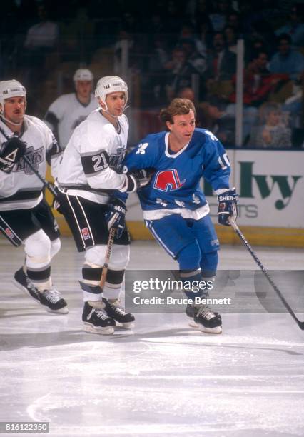 Guy Lafleur of the Quebec Nordiques skates on the ice as Tony Granato of the Los Angeles Kings grabs onto him during an NHL game circa 1990 at the...