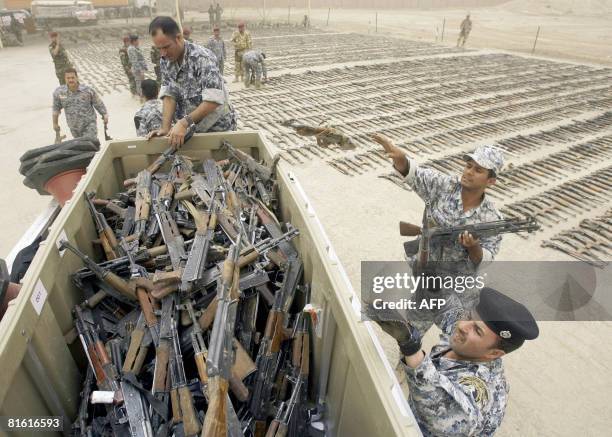 Iraqi policemen clear away assault rifles seized by Iraqi security forces during recent operations in the Shiite enclave of Sadr City that were...