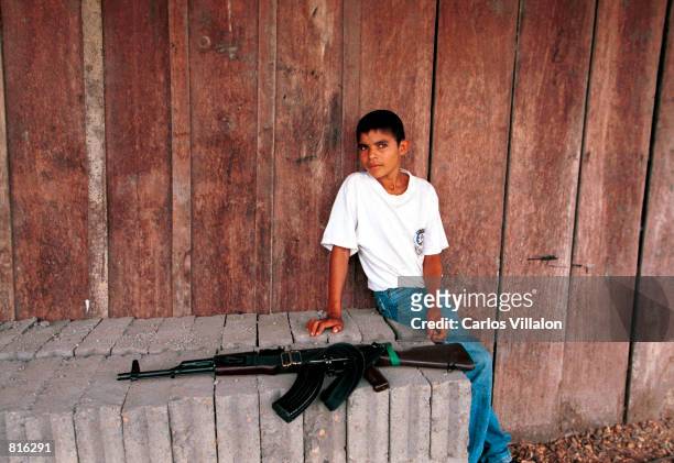 Boy sits near an AK-47 assault rifle at a FARC check point February 26, 2001 in Cristales, Colombia. The FARC is the country's largest rebel group...