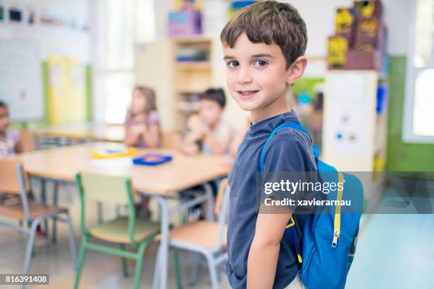 cute schoolboy carrying backpack in classroom - school boy with bag stock pictures, royalty-free photos & images