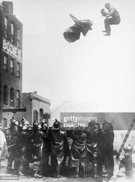 Fireman trapped in the upper floor of a burning building leaps onto a safety net held by his colleagues in Newark, New Jersey, circa 1925. He has...