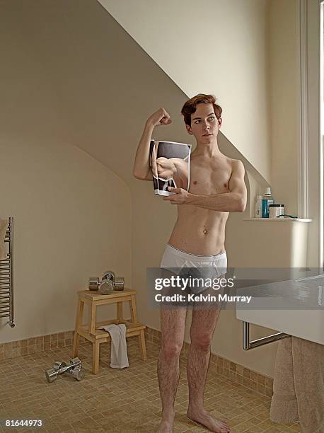 Young man in bathroom, holding up picture.